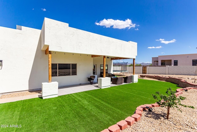 rear view of property with a trampoline, a patio, and a lawn