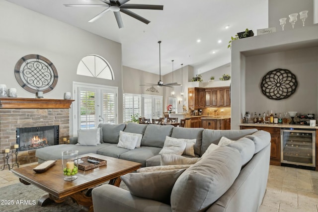 living area featuring beverage cooler, stone tile floors, ceiling fan, a bar, and high vaulted ceiling