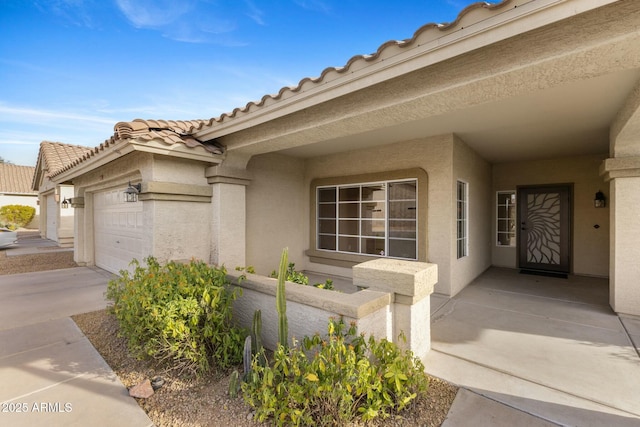 property entrance featuring a garage, a tiled roof, concrete driveway, and stucco siding