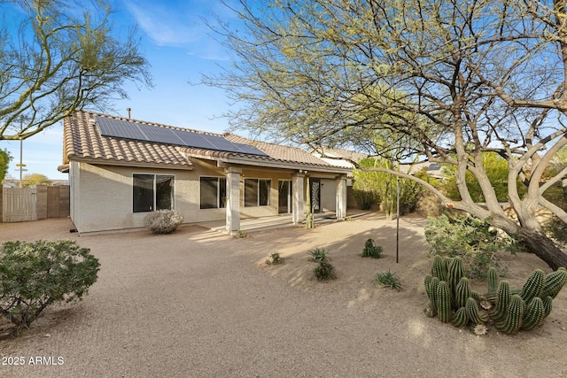 back of property with a tile roof, a patio, solar panels, stucco siding, and fence