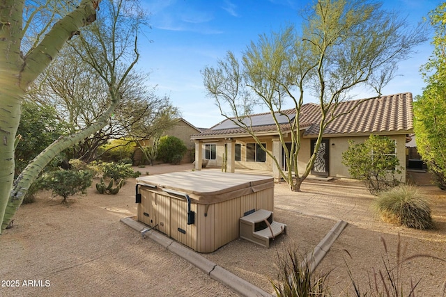 rear view of house with a hot tub, a patio, a tiled roof, roof mounted solar panels, and stucco siding