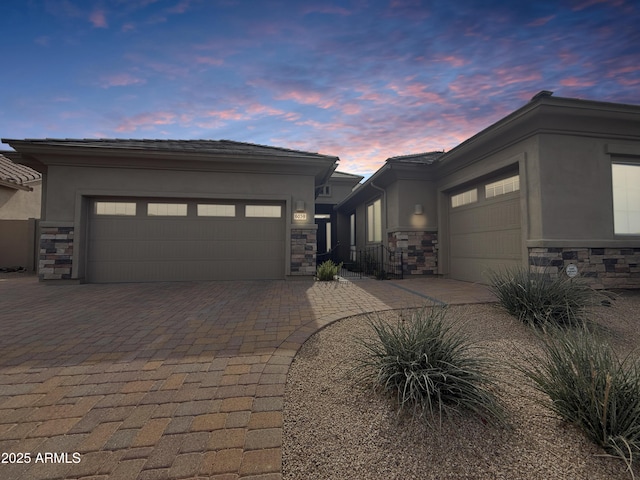 prairie-style house featuring a garage, stone siding, decorative driveway, and stucco siding