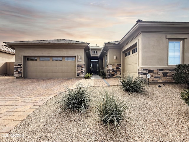 view of front of home with a garage, stone siding, decorative driveway, and stucco siding