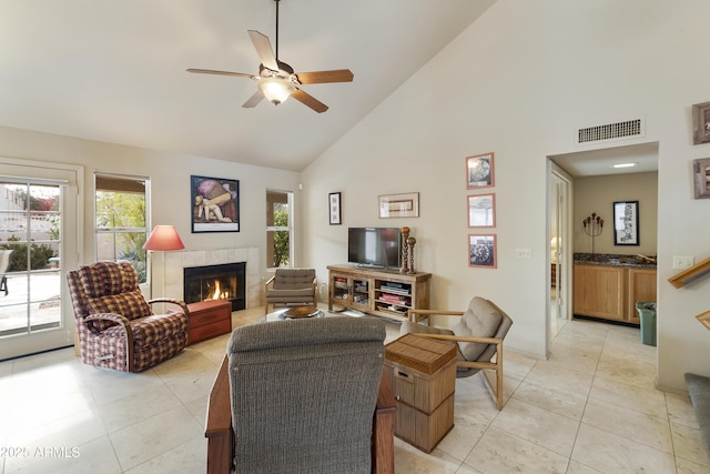 tiled living room with ceiling fan, high vaulted ceiling, and a tile fireplace