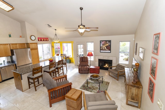 living room featuring a tiled fireplace, vaulted ceiling, light tile patterned flooring, and ceiling fan