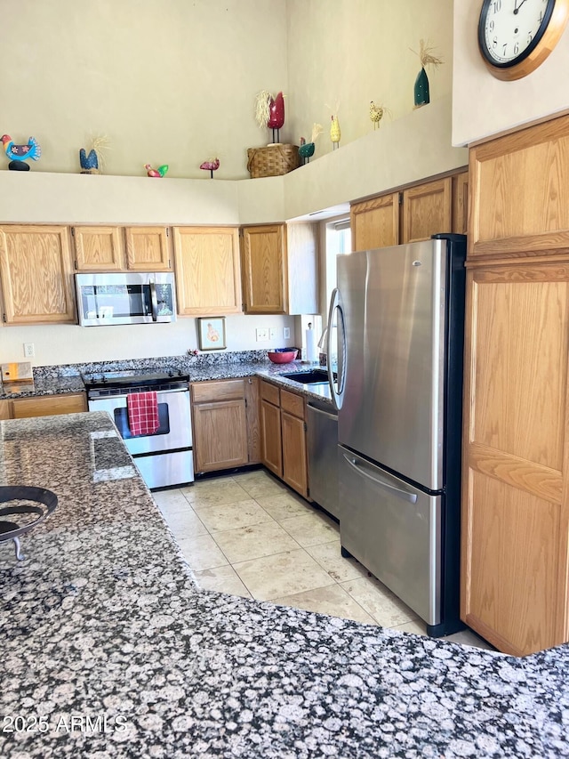 kitchen featuring light tile patterned floors, a towering ceiling, dark stone counters, and appliances with stainless steel finishes