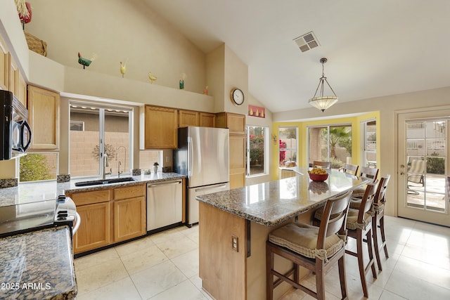 kitchen with sink, a center island, hanging light fixtures, dark stone countertops, and stainless steel appliances