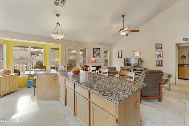 kitchen with light tile patterned floors, dark stone countertops, hanging light fixtures, a kitchen island, and light brown cabinets