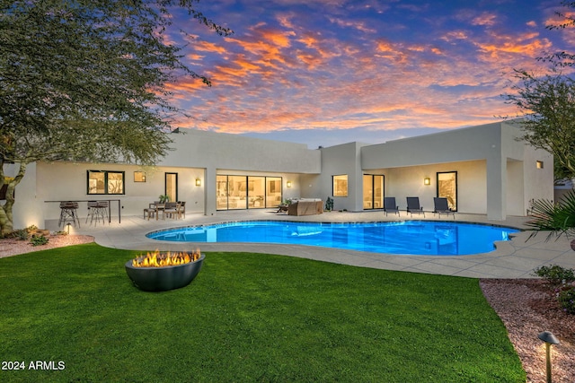 pool at dusk featuring a lawn and a patio