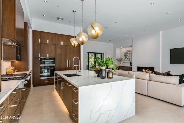 kitchen featuring stainless steel gas stovetop, a large island with sink, sink, wall chimney exhaust hood, and decorative light fixtures