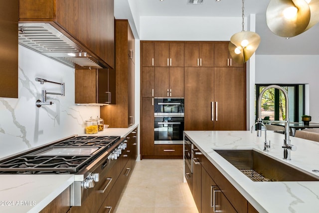 kitchen featuring pendant lighting, stainless steel gas stovetop, sink, light stone counters, and custom range hood