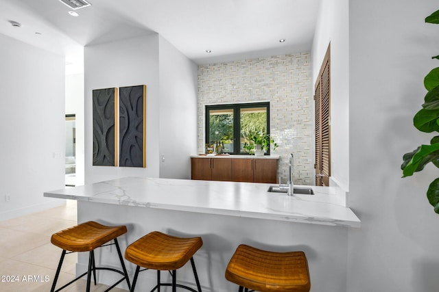 kitchen with kitchen peninsula, a kitchen breakfast bar, light tile patterned floors, and sink