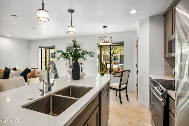 kitchen with sink, light stone counters, pendant lighting, decorative backsplash, and appliances with stainless steel finishes