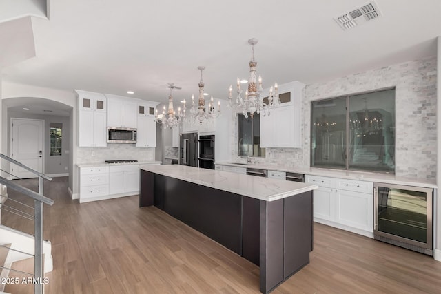 kitchen with appliances with stainless steel finishes, white cabinetry, wine cooler, and a kitchen island