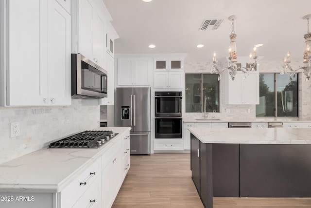 kitchen with appliances with stainless steel finishes, light stone counters, decorative light fixtures, an inviting chandelier, and white cabinetry