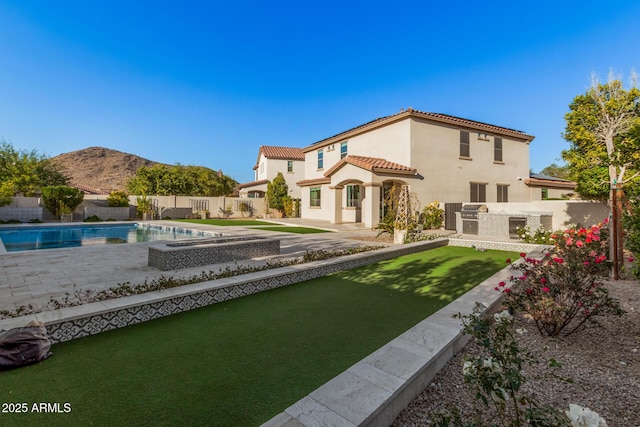 rear view of house with a mountain view, a fenced in pool, a patio area, and exterior kitchen