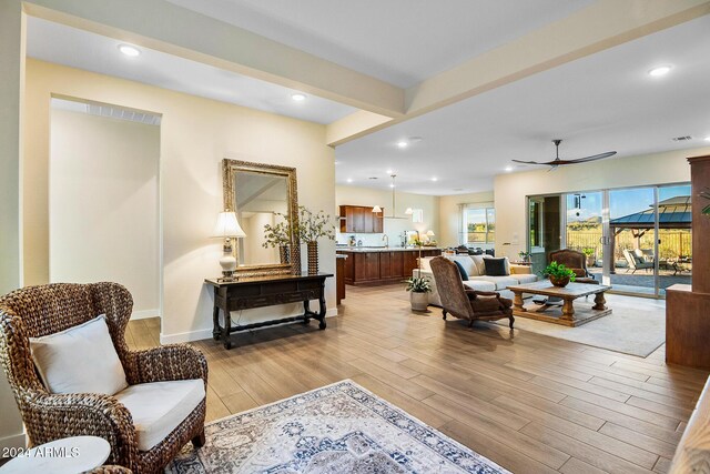 living room with ceiling fan, beam ceiling, and light hardwood / wood-style flooring