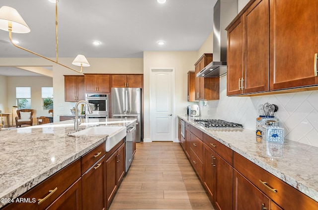 kitchen featuring wall chimney range hood, sink, hanging light fixtures, light hardwood / wood-style flooring, and light stone countertops