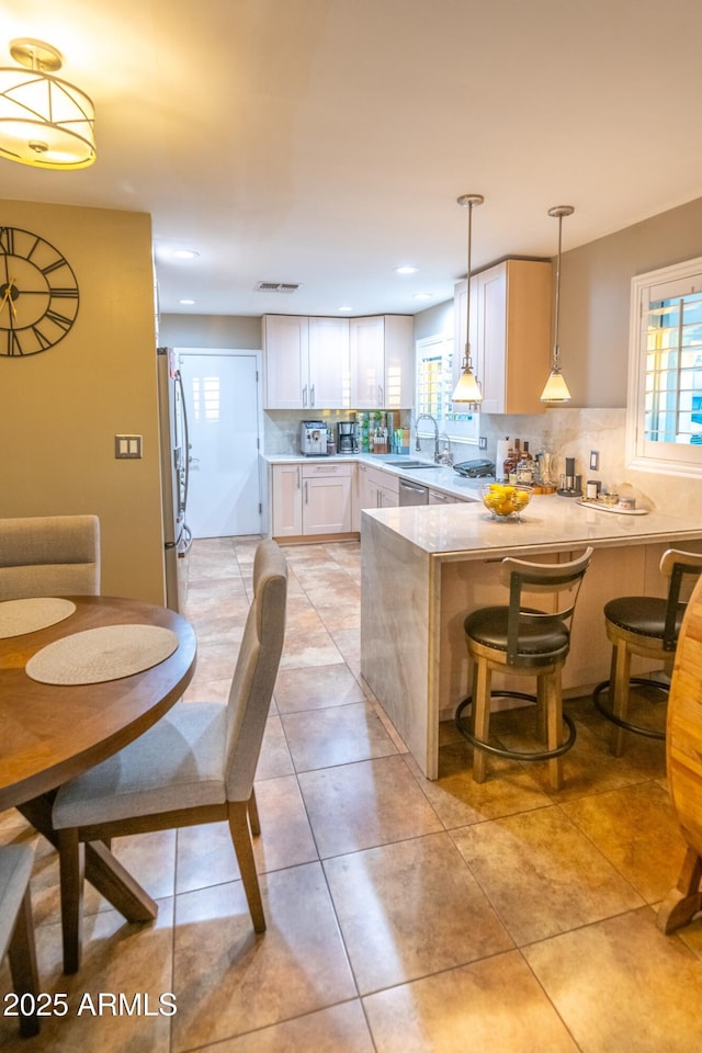 kitchen with sink, white cabinetry, decorative light fixtures, fridge, and kitchen peninsula