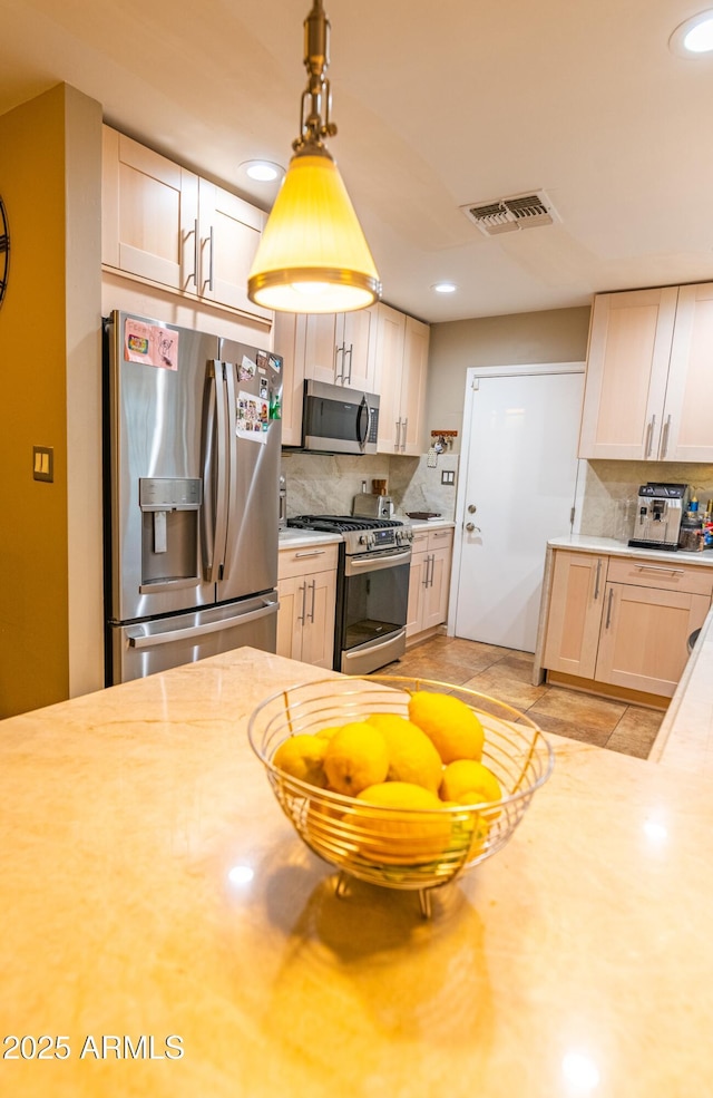 kitchen with pendant lighting, appliances with stainless steel finishes, tasteful backsplash, and light brown cabinets