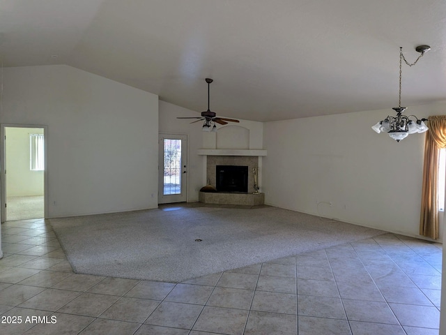 unfurnished living room featuring light carpet, a fireplace with raised hearth, ceiling fan with notable chandelier, light tile patterned floors, and vaulted ceiling