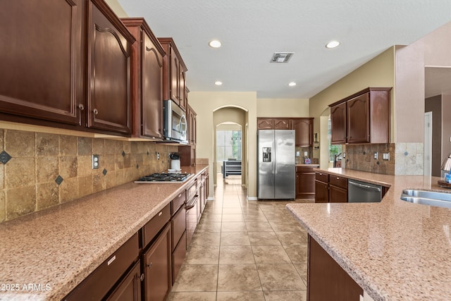 14430 W Windsor Ave, Goodyear, AZ 85395 - kitchen with stainless steel appliances, arched walkways, a sink, light stone counters, and tasteful backsplash