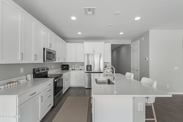 kitchen with sink, a kitchen island with sink, appliances with stainless steel finishes, dark hardwood / wood-style floors, and a kitchen bar