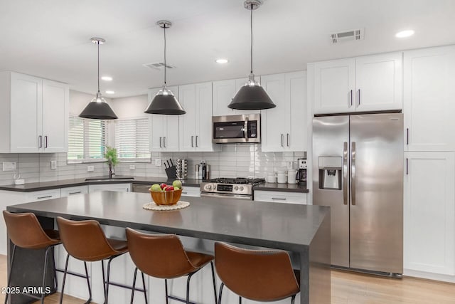 kitchen featuring decorative light fixtures, stainless steel appliances, white cabinets, and a kitchen island