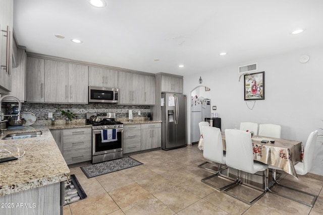 kitchen featuring gray cabinets, visible vents, tasteful backsplash, a sink, and stainless steel appliances