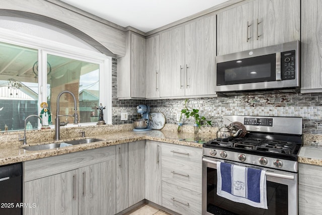 kitchen with light stone countertops, appliances with stainless steel finishes, a sink, decorative backsplash, and modern cabinets