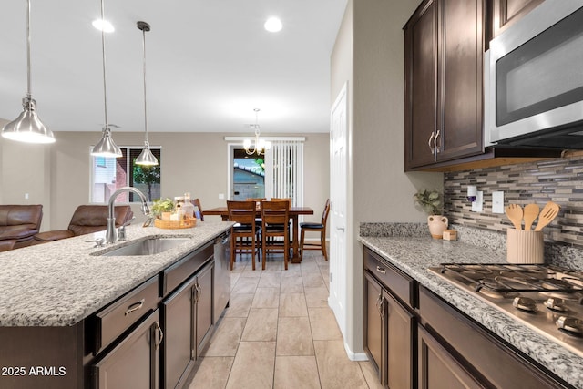 kitchen with a sink, light stone counters, tasteful backsplash, stainless steel appliances, and dark brown cabinets