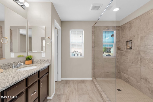 bathroom featuring visible vents, baseboards, vanity, and a walk in shower