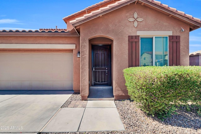 property entrance featuring stucco siding, a tiled roof, driveway, and a garage