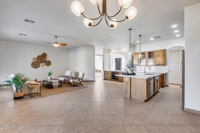 kitchen with a center island with sink, arched walkways, glass insert cabinets, light countertops, and a sink