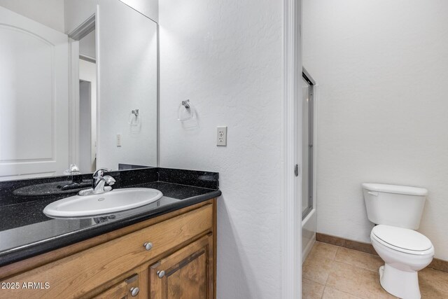 bathroom with toilet, enclosed tub / shower combo, vanity, baseboards, and tile patterned floors