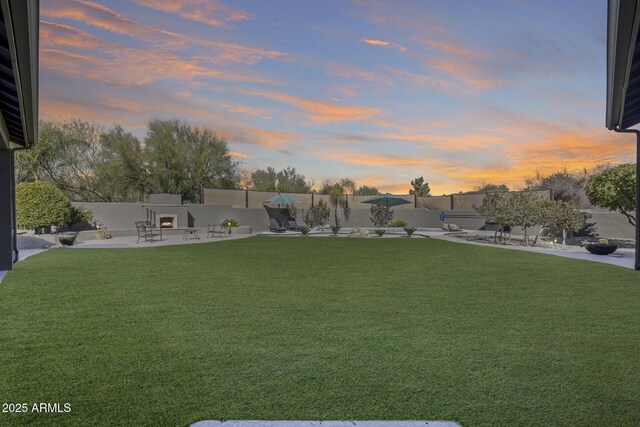 view of yard with a warm lit fireplace, a fenced backyard, and a patio area