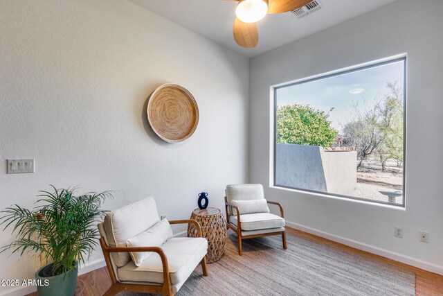 living area featuring a ceiling fan, wood finished floors, visible vents, and baseboards