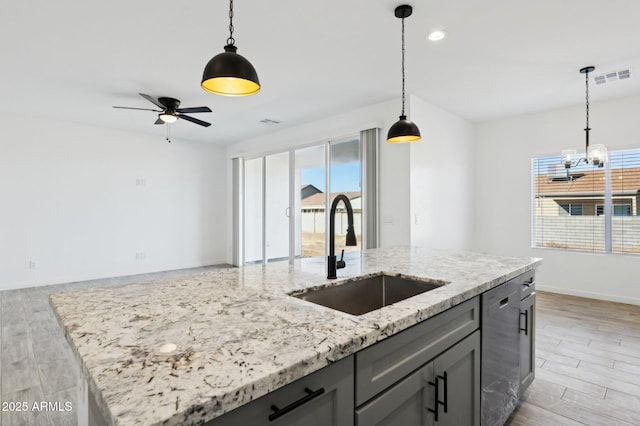 kitchen with light stone countertops, dishwasher, decorative light fixtures, sink, and a center island with sink