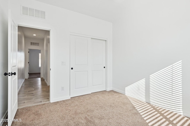 unfurnished bedroom with light colored carpet and a closet