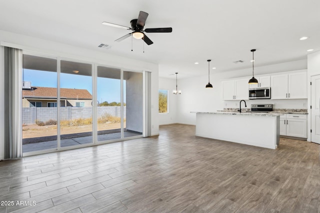 kitchen featuring hanging light fixtures, white cabinets, appliances with stainless steel finishes, and light stone counters