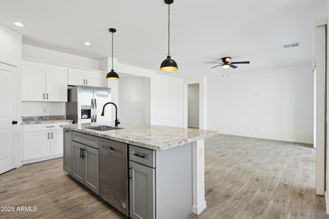 kitchen with white cabinetry, an island with sink, stainless steel appliances, decorative light fixtures, and light stone countertops