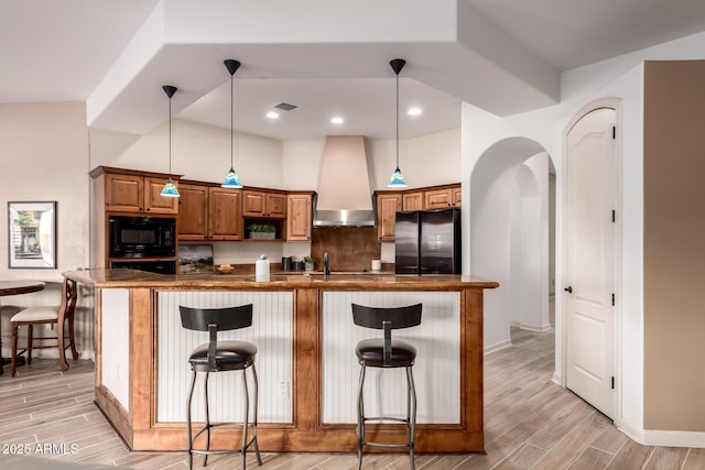 kitchen with a breakfast bar, hanging light fixtures, tasteful backsplash, black appliances, and wall chimney exhaust hood