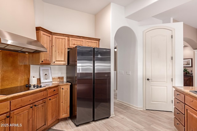 kitchen featuring wall chimney range hood, stainless steel fridge, black electric cooktop, and light hardwood / wood-style floors