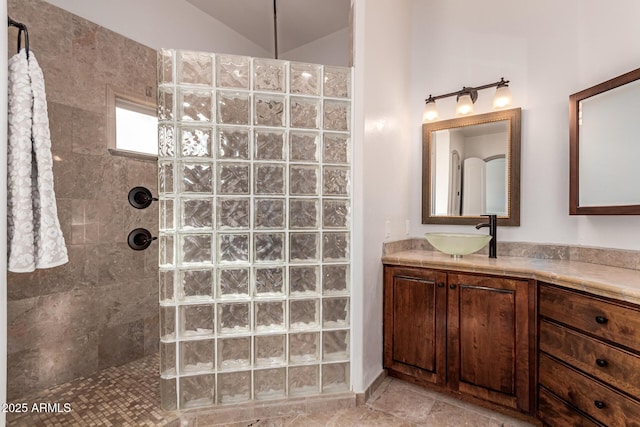 bathroom featuring tiled shower, vanity, and lofted ceiling