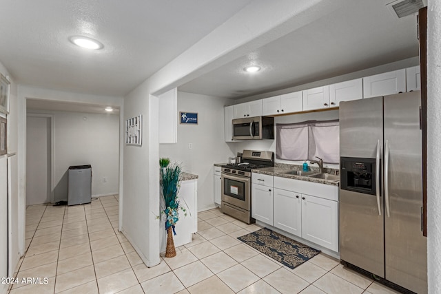 kitchen featuring white cabinets, light tile patterned floors, sink, stainless steel appliances, and dark stone counters