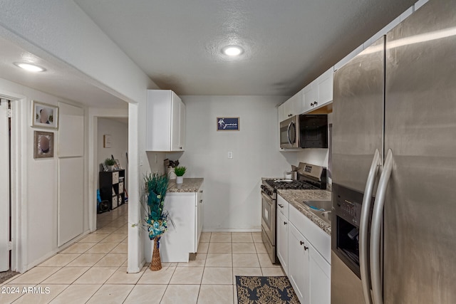 kitchen featuring white cabinets, light tile patterned floors, stone countertops, a textured ceiling, and stainless steel appliances