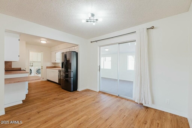 kitchen with washer and dryer, white cabinetry, light wood-type flooring, a textured ceiling, and black refrigerator with ice dispenser