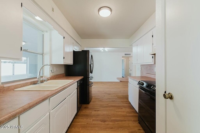 kitchen featuring sink, white cabinets, light wood-type flooring, and black appliances