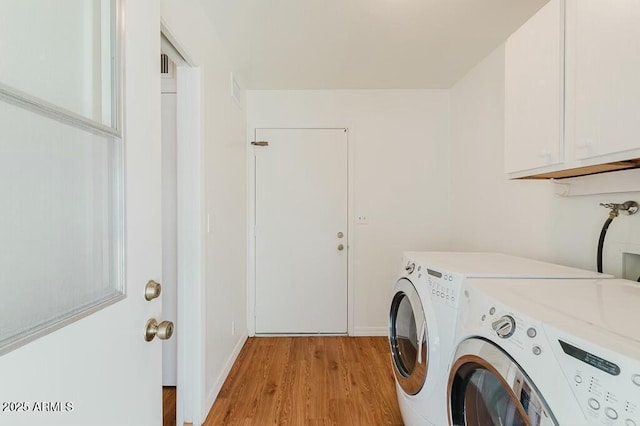 clothes washing area with cabinets, washing machine and dryer, and light hardwood / wood-style flooring