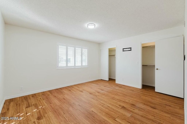 unfurnished bedroom with multiple closets, a textured ceiling, and light wood-type flooring